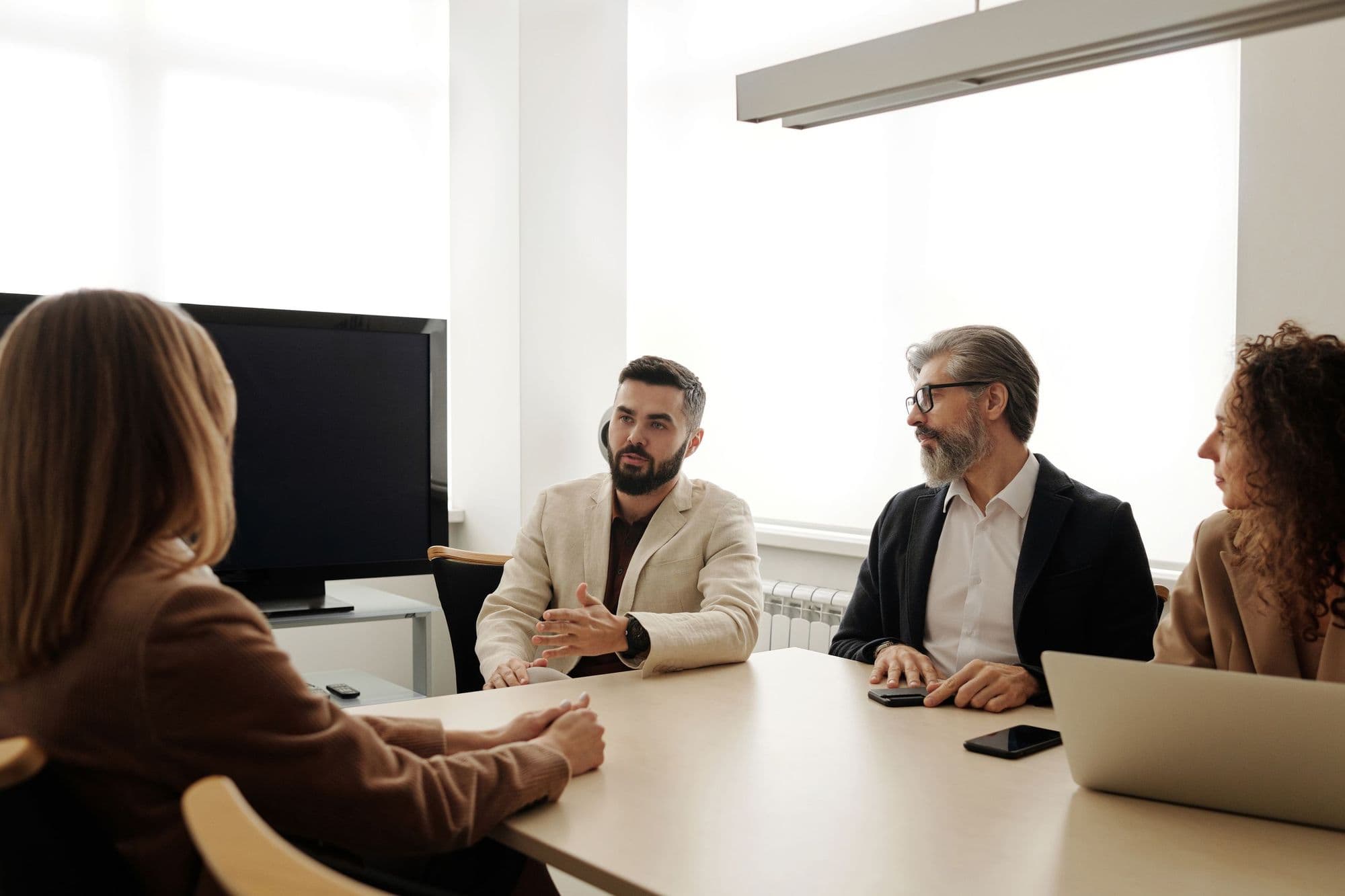 Four colleagues meet around a table in a bright office, a laptop open between them.