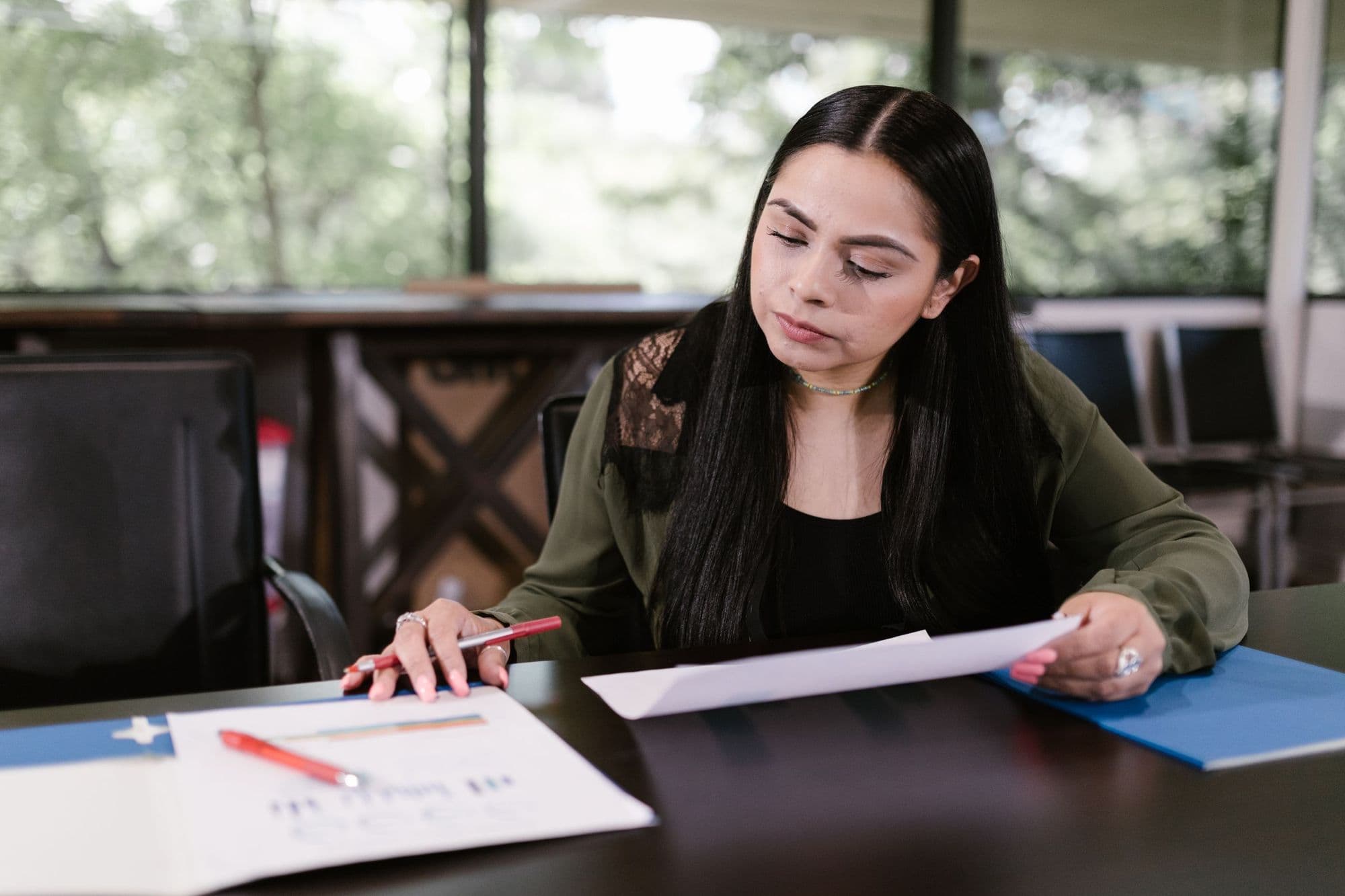 A woman reads through financial documents with a pen in hand at an office table.