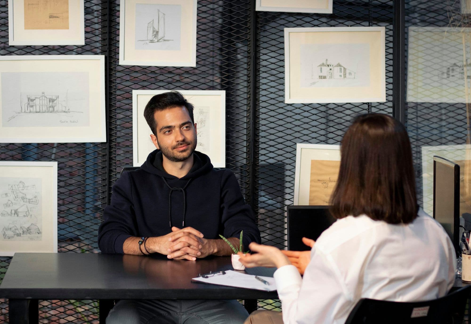 A job interview across a desk: a young man listens while the interviewer talks him through the role.