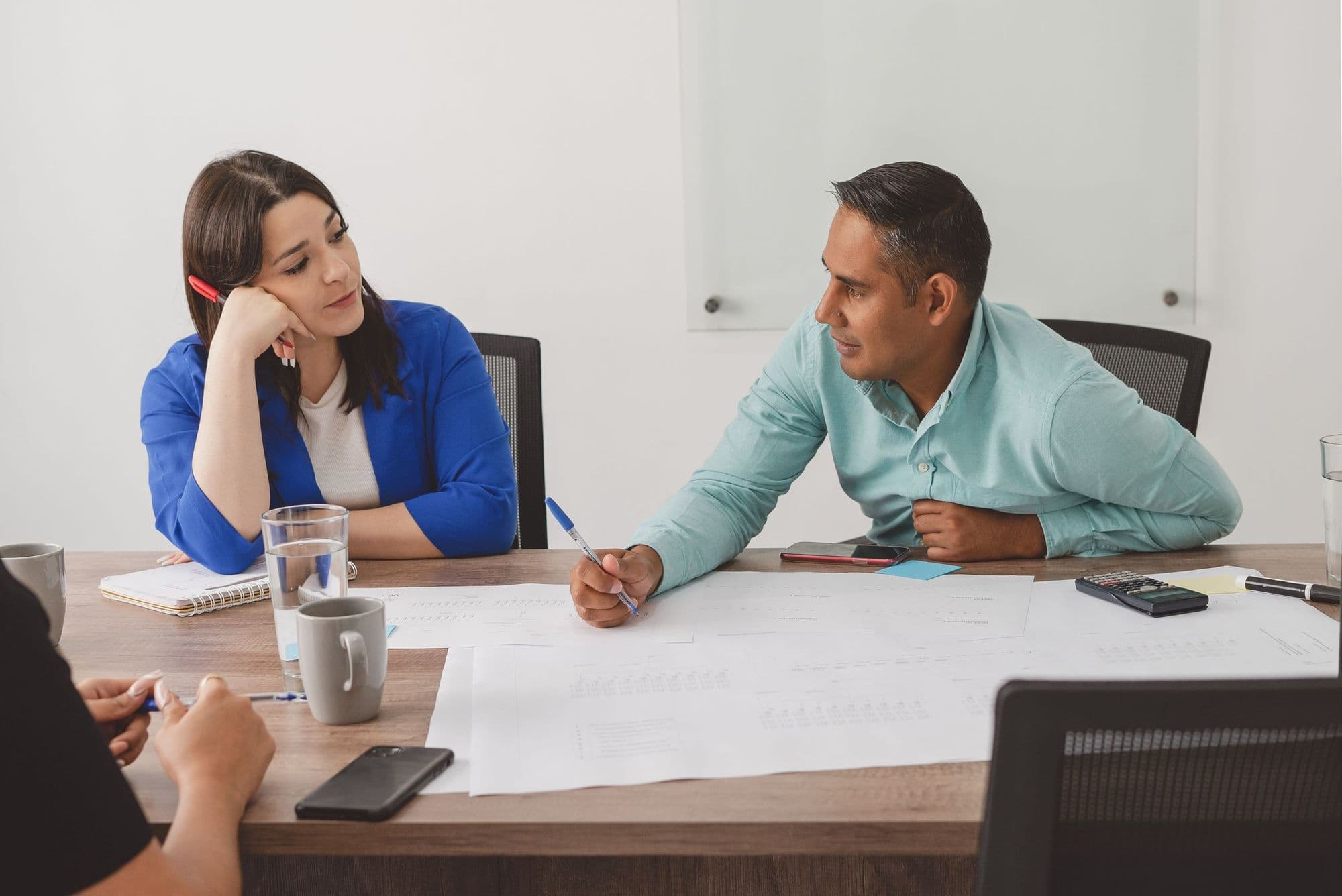 Two colleagues go through a set of documents together at a meeting table.
